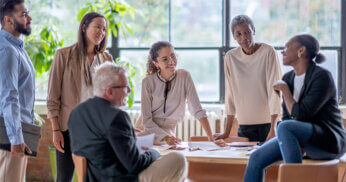 Group of diverse professionals sitting in an office talking with one another.