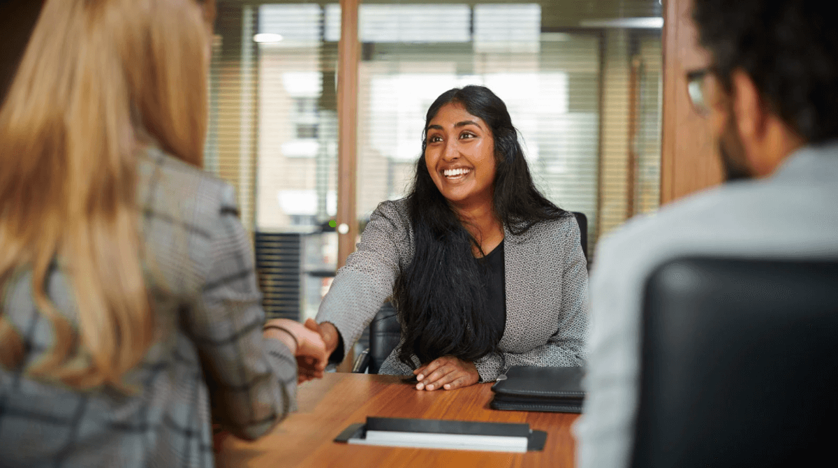 Candidate smiling while shaking hands with an interviewer in a modern office setting, representing successful SEO hiring outcomes.