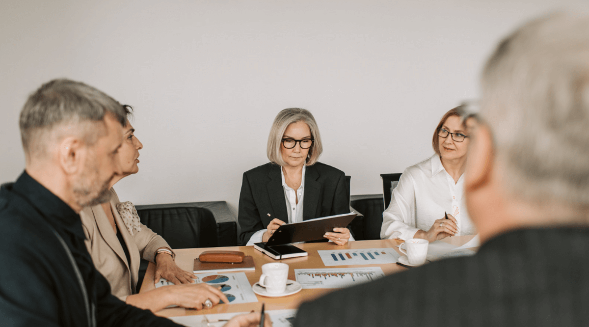 Senior business leaders in a conference room reviewing reports and charts during a strategic planning meeting focused on performance, data analysis, and decision-making.