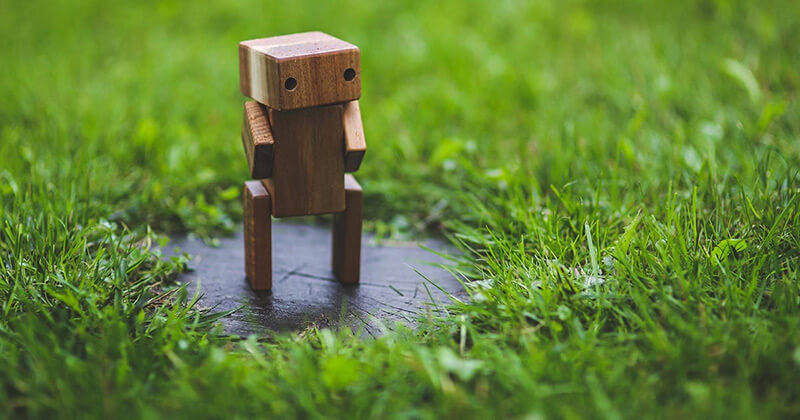 Wooden robot figure stands on a patch of grass.