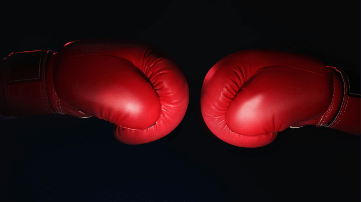 Two red boxing gloves facing each other against a dark background, symbolizing competition or a head-to-head comparison.