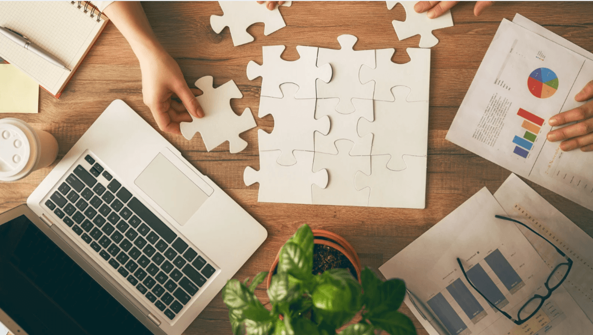 A desk with a laptop and an unfinished puzzle on top of it.