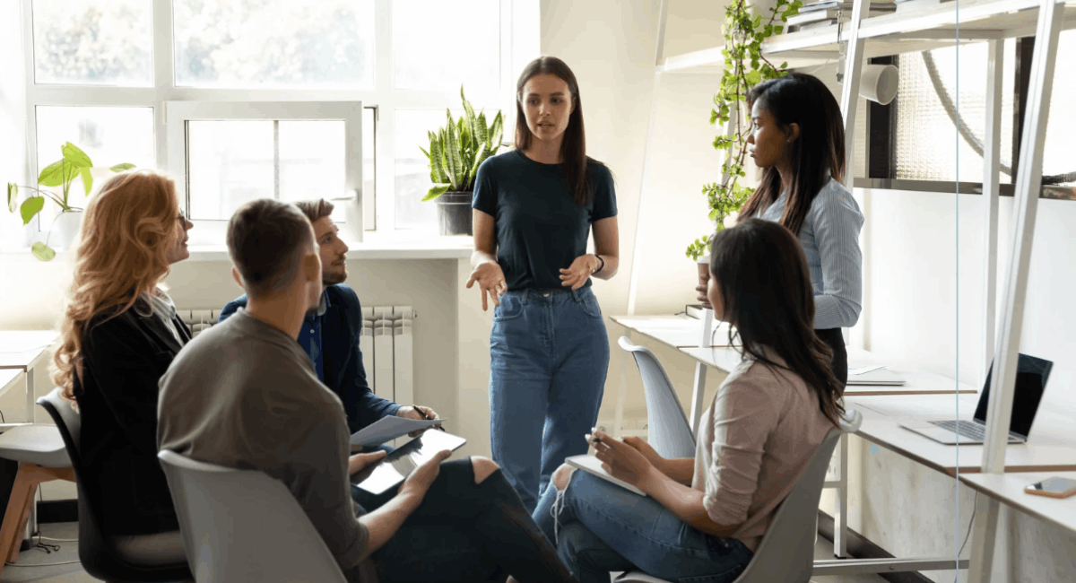 A group of diverse professionals having a collaborative discussion in a bright, modern office with plants and industrial shelving.