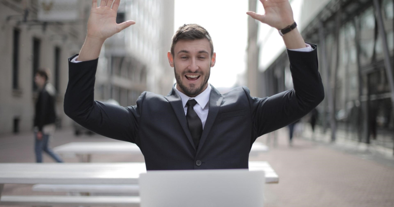 Man in suit looking at laptop with hands up, winning at SEO.