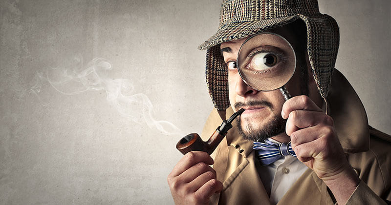 Man wearing detective clothing looking through magnifying glass.