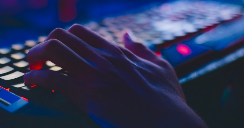 A hand types on a keyboard in a dark room.