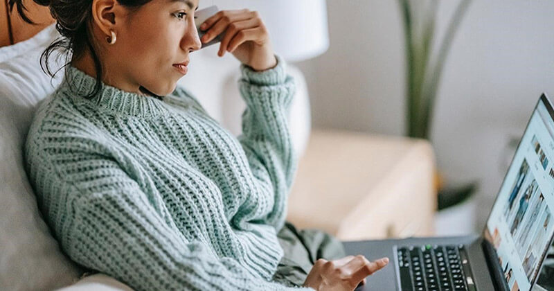 Woman sits on couch browsing online store on her laptop.