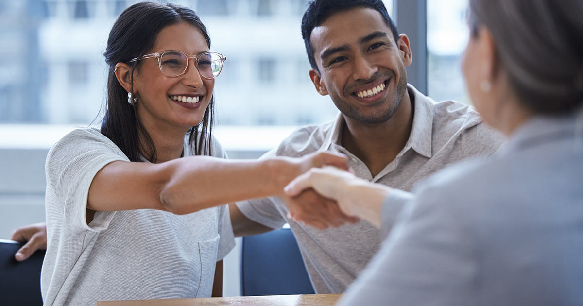 mortgage broker shaking hands with smiling happy couple.