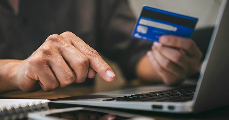 man holding credit card making online purchase on laptop.