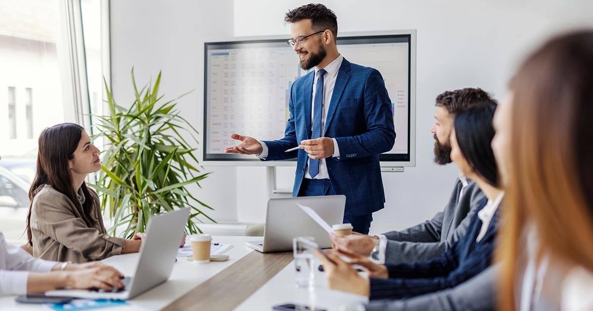 professional standing, training a team sitting around a conference table.
