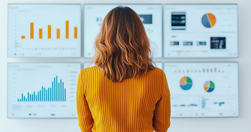 A woman reviews multiple marketing dashboard screens displaying various graphs and charts.
