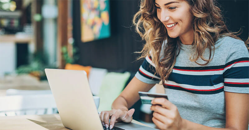 smiling woman holding credit card making purchase on laptop.