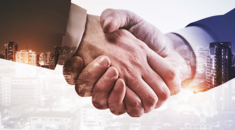 Close-up of a firm handshake between two people wearing business suits, overlaid with a city skyline at sunset symbolizing partnership and collaboration.