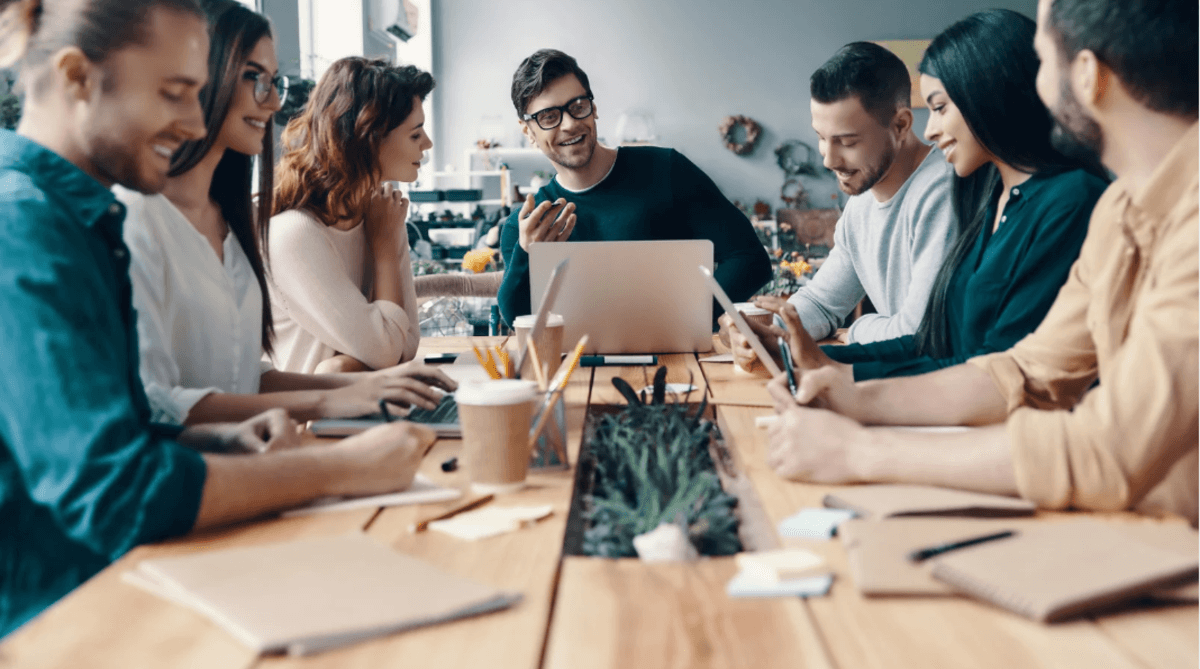 Content team collaborating around a table with laptops and notebooks, discussing digital strategy in a modern office.