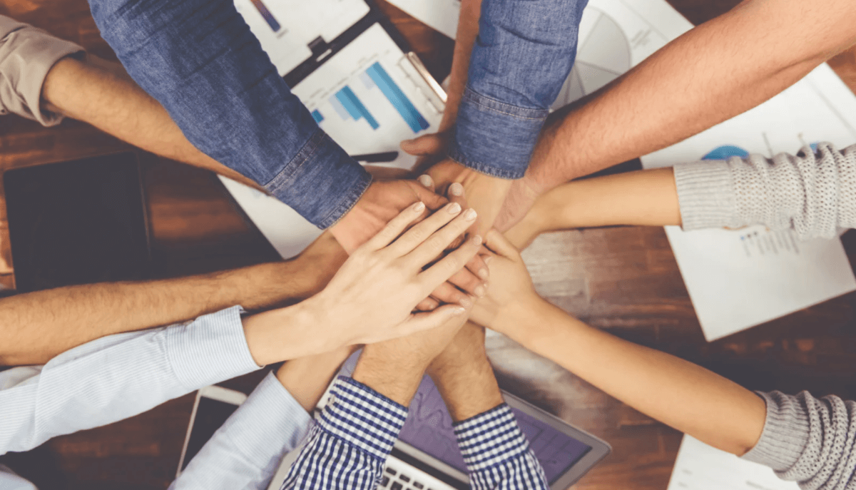Marketing and content team joining hands in the center of a table to show teamwork and collaboration on SEO projects.