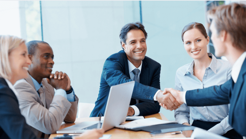 Executives in a conference room shaking hands during a business meeting, symbolizing agency partnerships and outsourced SEO collaboration.