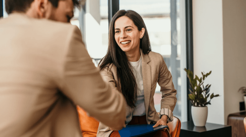 Professional woman smiling and holding a clipboard during a job interview, illustrating positive hiring experiences in SEO recruitment.