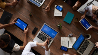 Overhead view of a marketing team collaborating at a conference table using laptops, tablets, and smartphones to review digital strategy and analytics.