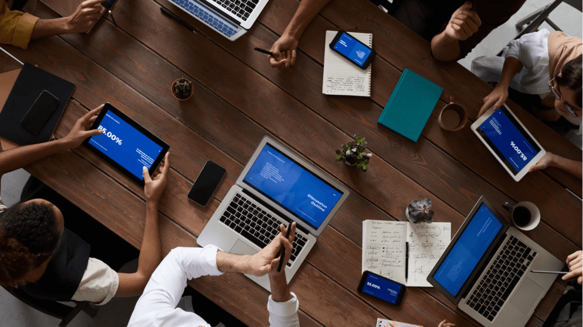 Overhead view of a marketing team collaborating at a conference table using laptops, tablets, and smartphones to review digital strategy and analytics.