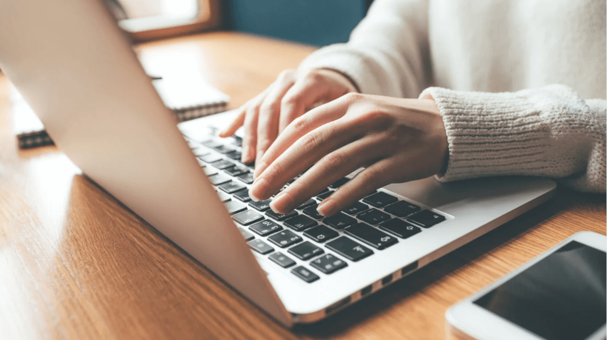 Close-up of hands typing on a laptop computer at a desk, representing content creation, digital marketing work, and AI-assisted productivity.