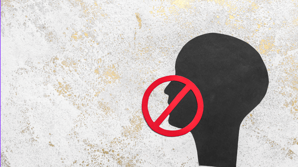 Black human head silhouette overlaid with a red ‘no’ symbol on a textured background, representing censorship or restricted speech.