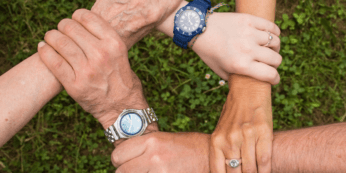Top-down view of four arms of varying ages—representing Baby Boomers, Gen X, Millennials, and Gen Z—grasping each other's wrists in a square formation over grass, symbolizing cross-generational connection and unity.