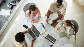 Overhead view of a team collaborating around a table with laptops, notebooks, and wireframe sketches during a UX planning session
