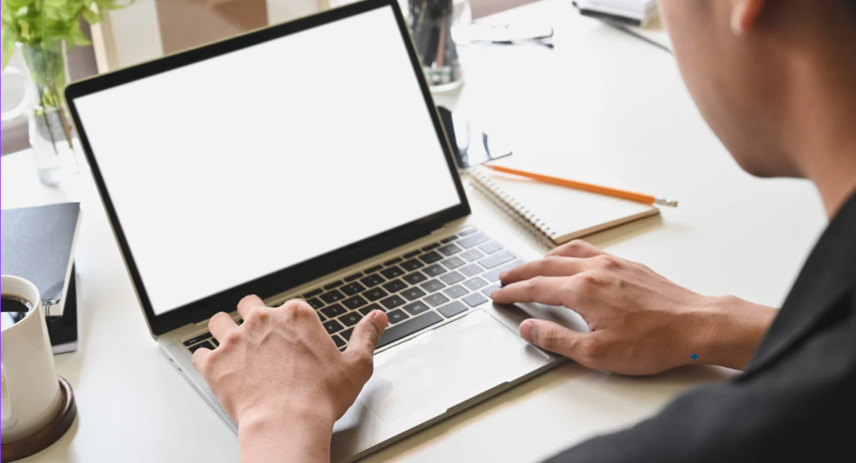 Person typing on a laptop at a desk with coffee and notebook in a home office workspace