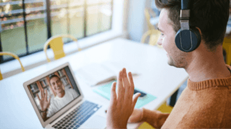 Remote business meeting with two professionals on a video call, one wearing headphones and waving at a colleague on a laptop screen