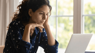 A focused woman with curly hair resting her chin on her hands while reading on a laptop, illustrating a user engaged in deep online research or digital content consumption.