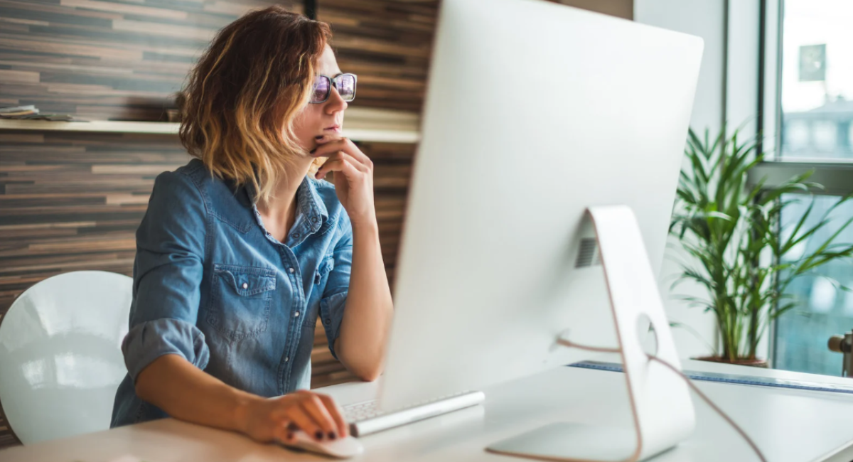 Woman working at a desktop computer in a modern office with natural light and plants