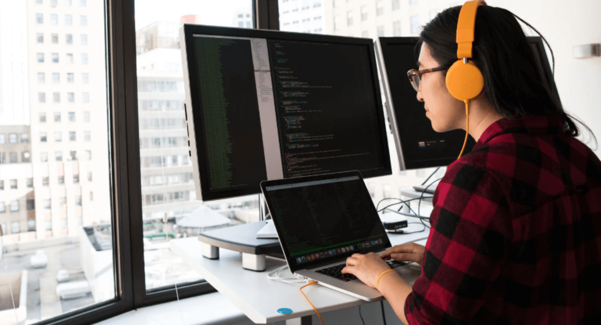 Developer wearing headphones reviewing code on multiple monitors while debugging technical SEO and crawl errors