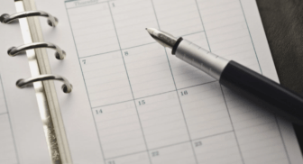 A close-up of a high-quality fountain pen resting on an open paper planner or calendar page, symbolizing scheduling and consistency.