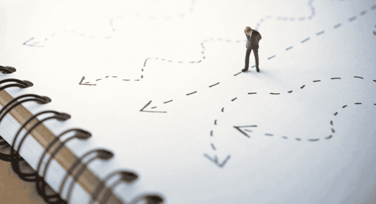 A miniature figurine of a businessman standing on a notebook surrounded by hand-drawn dashed lines and arrows pointing in various directions.