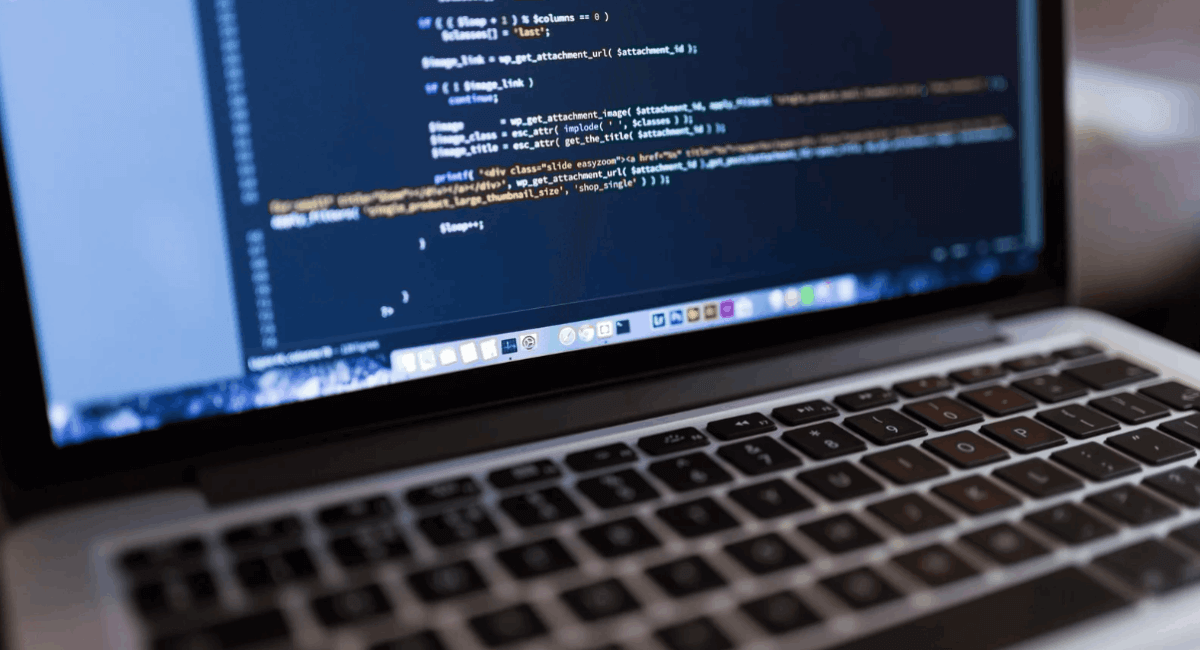Close-up of a laptop screen displaying rows of clean programming code, including PHP and HTML tags, in a dark-themed text editor.