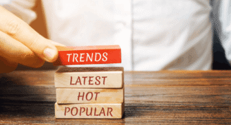 A hand placing a red wooden block labeled "TRENDS" on top of a stack of blocks labeled "LATEST," "HOT," and "POPULAR."