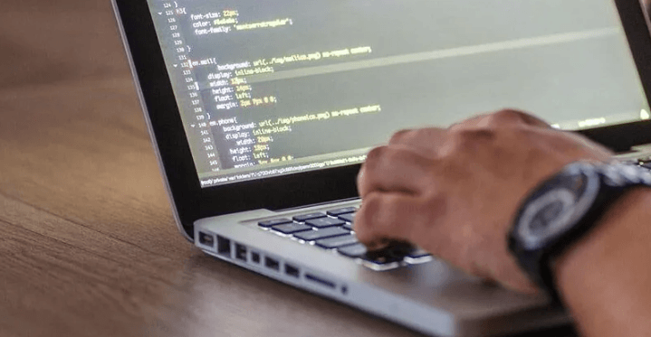 The Always Up-to-Date SEO Checklist插图7 Close-up of a person's hand wearing a watch as they type on a laptop keyboard, with lines of programming code visible on the screen.