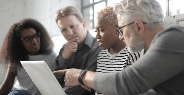 The Always Up-to-Date SEO Checklist插图12 A group of four diverse professionals huddled together looking closely at a laptop screen while an older man points at the display.