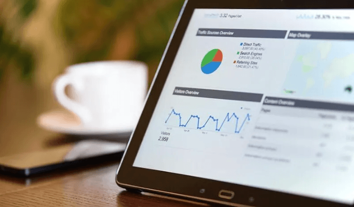 The Always Up-to-Date SEO Checklist插图11 A close-up view of a tablet screen displaying a web analytics dashboard featuring traffic source pie charts, a visitor overview line graph, and data metrics next to a white coffee cup.